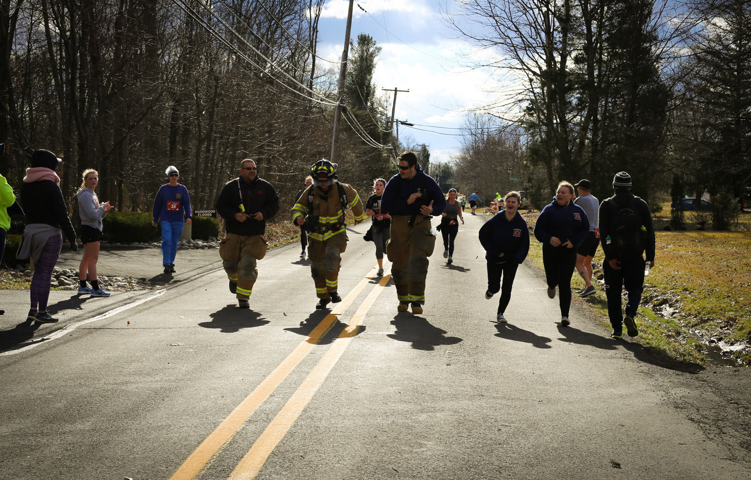 Firefighters in full turnout gear running the Blaze of Glory 5K along a tree-lined Plumsteadville road